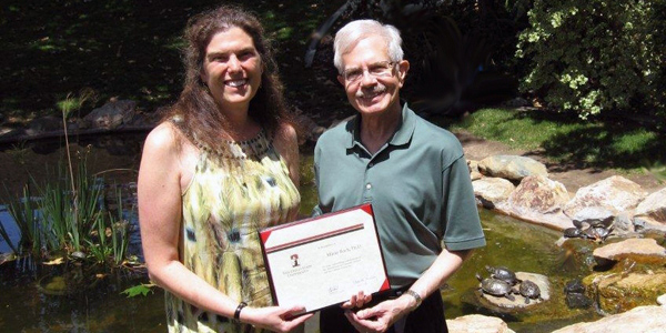 Dr. Leland Beck giving Dr. Marie Roch an awards with grass in background.